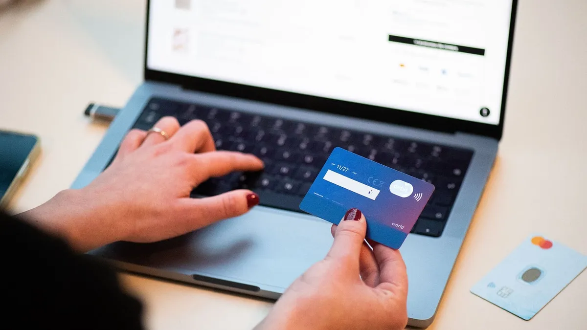A person holding a bank card while shopping on a laptop